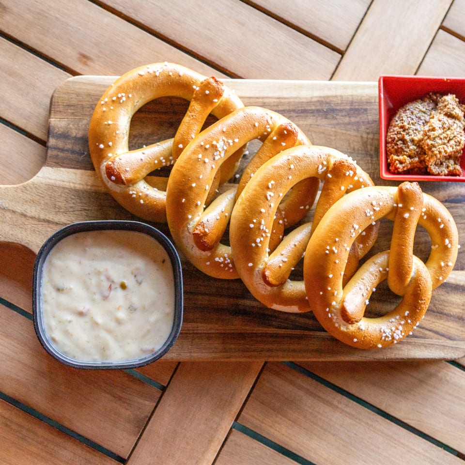 Salted soft pretzels on a wooden serving board with creamy dipping sauce and coarse mustard.