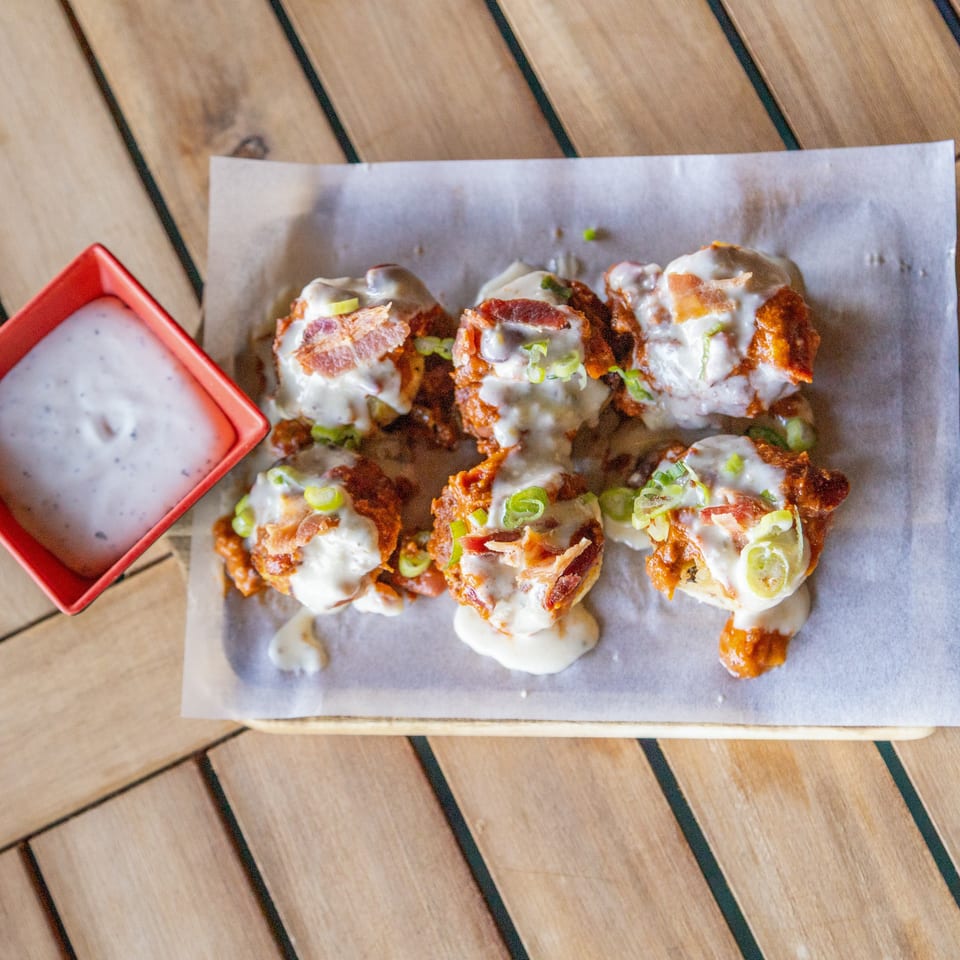 Crispy bacon-topped chicken pieces with melted cheese and green onions, served with ranch dipping sauce on a wooden table.
