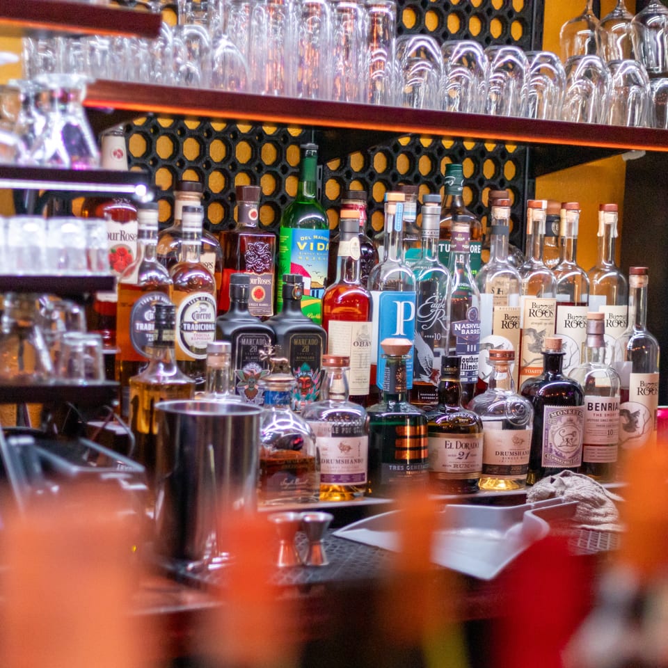 Well-stocked bar displays liquor bottles, cocktail tools, and rows of inverted glasses on wooden shelves.